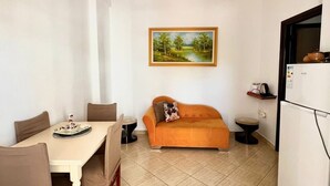 Un ambiente compatto con un tavolo da pranzo, sedie, un divano, un piccolo tavolino rotondo, un frigorifero e un quadro appeso al muro.