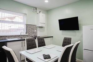 A modern kitchen with a built-in stove, a sink, and a window with blinds. There is a flat-screen TV mounted on the wall and a refrigerator to the right. - 6-bed Manchester Holiday (Manchester)