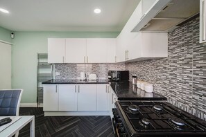 A modern kitchen with white cabinets, a black countertop, and a patterned backsplash. - 6-bed Manchester Holiday (Manchester)