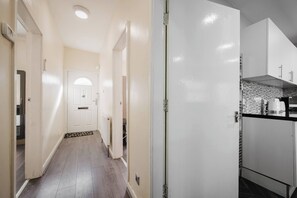 A narrow hallway with a door at the end, leading to a kitchen area with a tiled backsplash and a coffee maker on the counter. - 6-bed Manchester Holiday (Manchester)