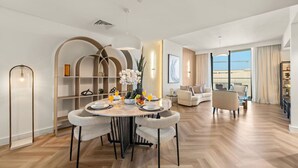 Uma sala de estar moderna com área de refeições, apresentando uma mesa redonda com cadeiras, um sofá e uma grande janela com vista.