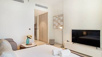 Een moderne hotelkamer met een groot bed, een flatscreen televisie, een klein nachtkastje met een vaas, en een gang die naar een deur leidt.