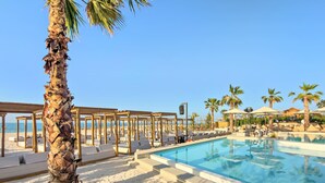 A poolside area with lounge chairs, a palm tree, and a clear blue sky. - FIRST CLASS | 3BR | Stunning Beachfront Bliss (Al Riffa)