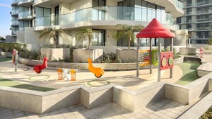A modern residential building with curved balconies and a children's play area with a red shelter. - FIRST CLASS | 3BR | Stunning Beachfront Bliss (Al Riffa)