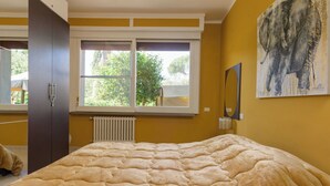 A bedroom with a large bed, a window with a view of greenery, a radiator, and a painting on the wall. - Atelier Vella by Interhome (Scarlino)