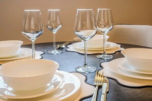 A dining table set with white bowls, plates, and wine glasses, with a fork and knife on the side. - Stylish Flat, Family Friendly, Walk to The Oracle (Reading)