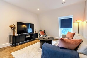 A modern living room with a flat-screen TV, black entertainment unit, round coffee table, and a sofa with cushions. - Stylish Flat, Family Friendly, Walk to The Oracle (Reading)