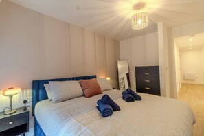 Un lit bien fait, avec des oreillers et des serviettes enroulées, une lampe de chevet et une œuvre d’art accrochée au mur.