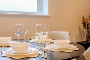 A dining table set with white bowls, wine glasses, and cutlery, with a vase of dried flowers on the side. - Stylish Flat, Family Friendly, Walk to The Oracle (Reading)