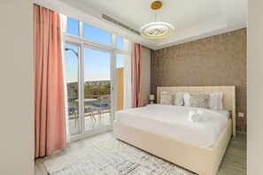 Habitación de hotel con una cama grande, un balcón con mesa y sillas, y vista a la ciudad.
