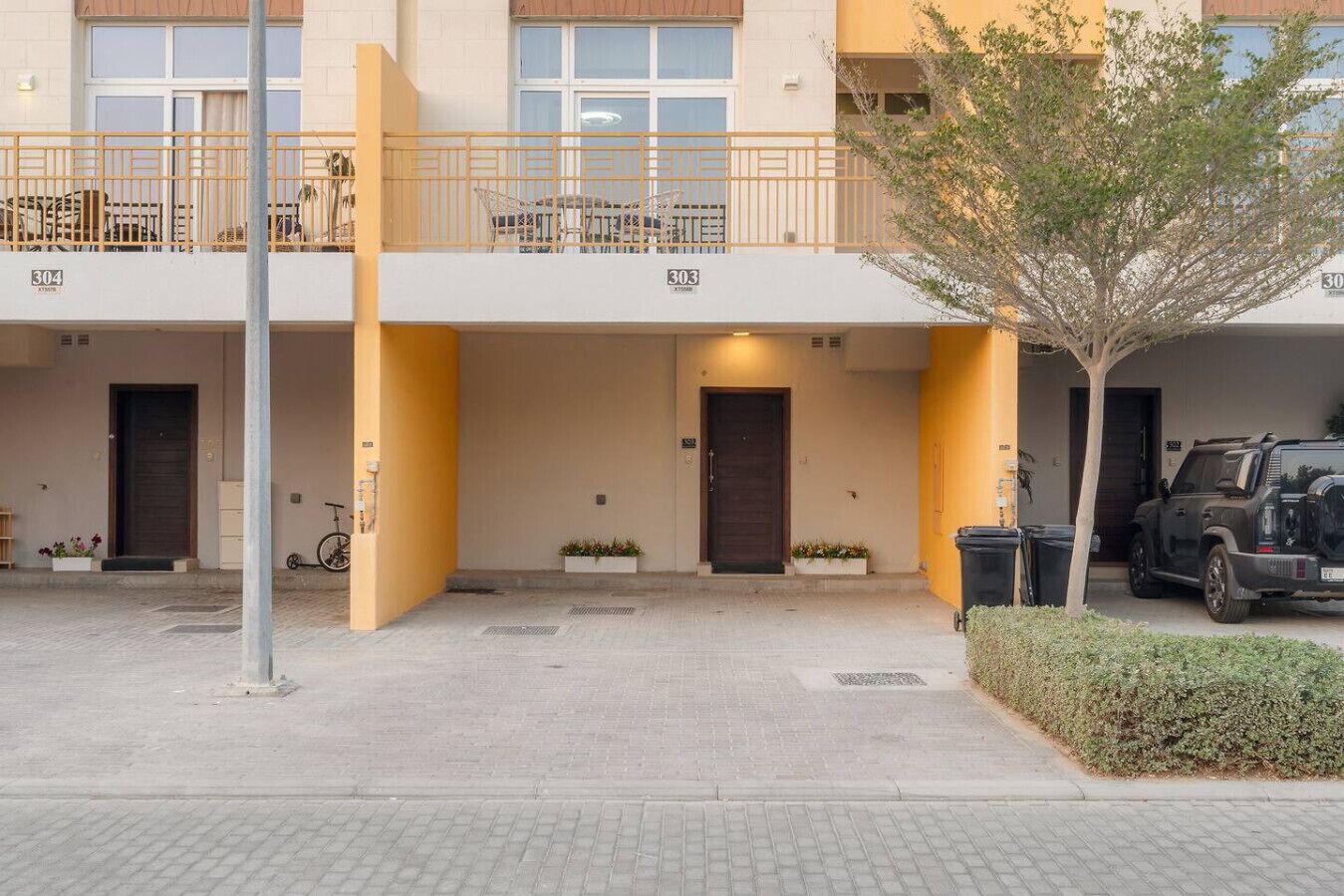 A building with a yellow facade, multiple doors, and a balcony with chairs.