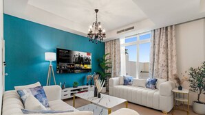 A modern living room with a teal accent wall, a chandelier, a sofa set, a coffee table, and a TV mounted on the wall.