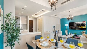 A modern dining area with a table set for four, a kitchen in the background, and a living area with a TV.