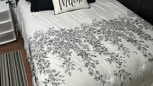 A neatly made bed with a floral-patterned duvet, a 'Welcome' pillow, and a wall-mounted decorative item above it. - Perfect 3-bedroom house with 2-car garage,AC and heat in welcoming Ponchatoula (Ponchatoula)