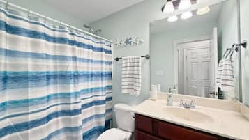 A bathroom with a striped shower curtain, a toilet, a sink with a mirror, and a towel rack.