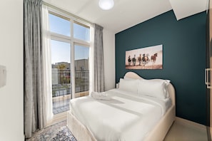 A bedroom with a large window, a bed, and a painting on the wall.