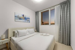 A hotel room with a bed, a nightstand, a lamp, a painting, and a window with curtains.