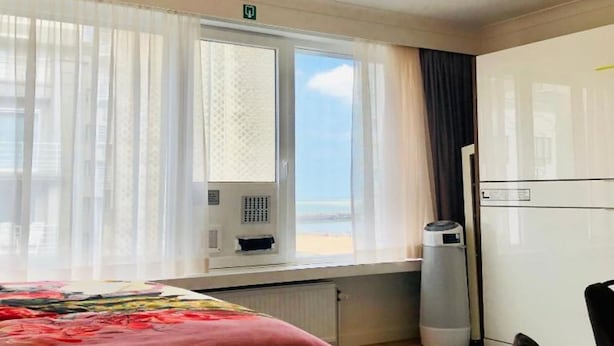 A hotel room with a bed, a desk, a chair, a window with curtains, and a ceiling light fixture. - Studio Oostende Dichtbij Strand Centrum (Ostend)