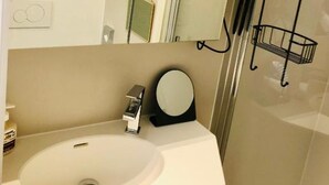 A bathroom with a white sink, a mirror, and a glass shower enclosure. - Studio Oostende Dichtbij Strand Centrum (Ostend)
