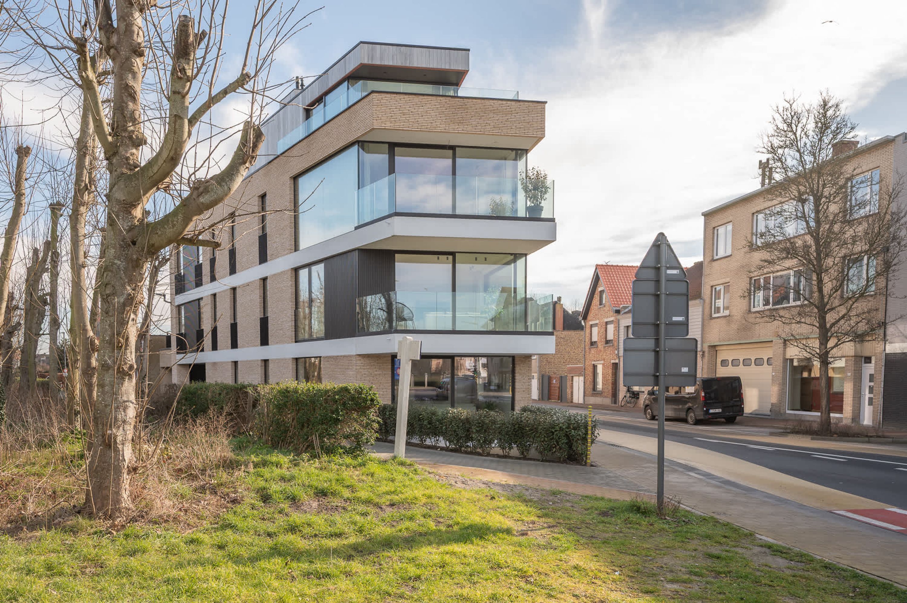 A modern multi-story building with large windows and a flat roof, surrounded by trees and a street.
