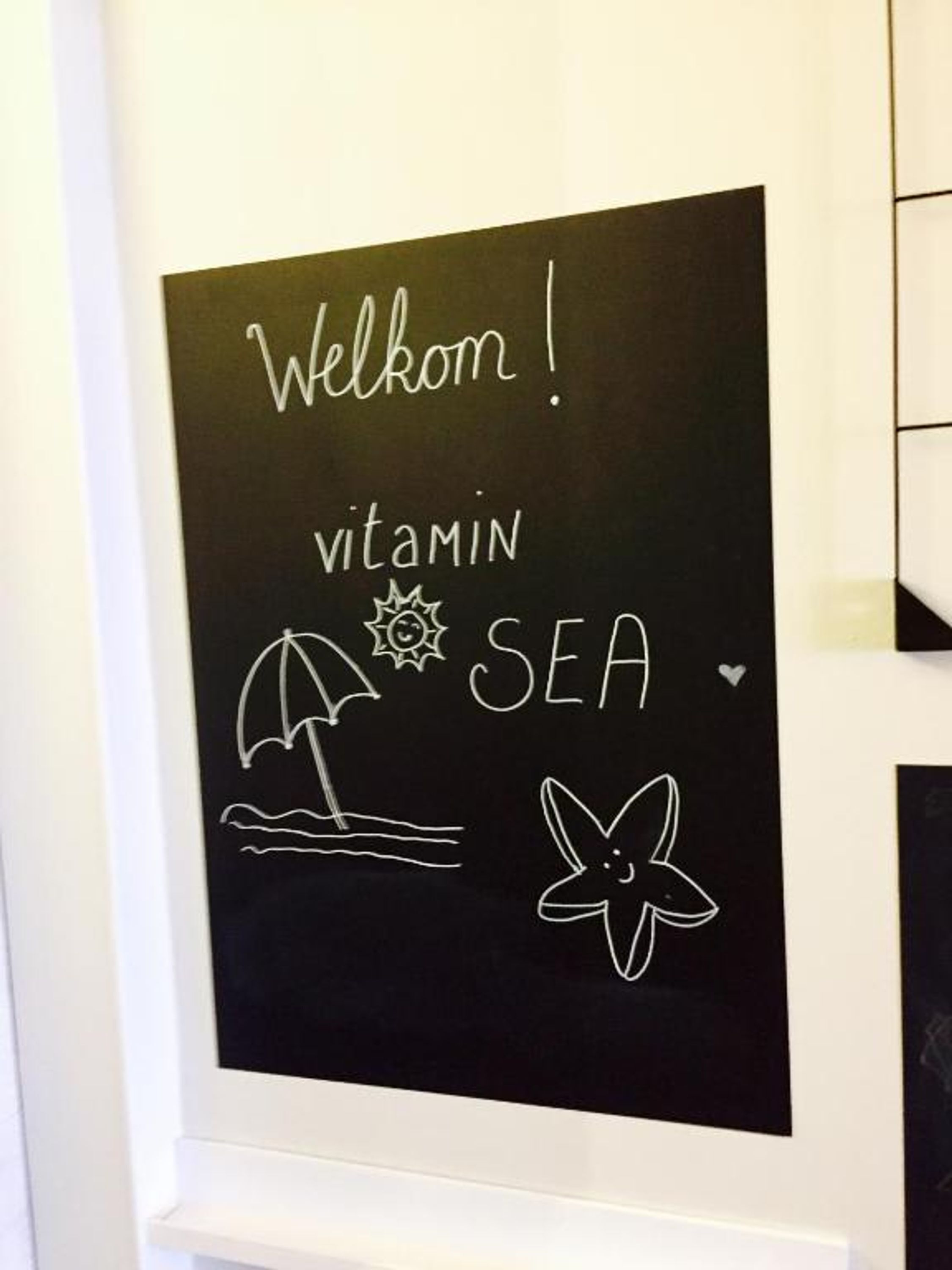 A blackboard with 'Welcome!' and 'vitamin SEA' written on it, along with a sun, waves, an umbrella, and a starfish drawing.