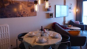 A dining area with a table set for four, a sofa, and a television mounted on the wall. - Zeezicht Studio Alisa (Blankenberge)