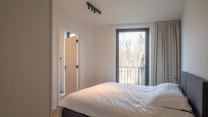 A bedroom with a bed, a window with curtains, and a door leading to another room. - Levant Appartement 2 Slaapkamers 2 Badkamers Balkon Knokke-heist (Knokke-Heist)