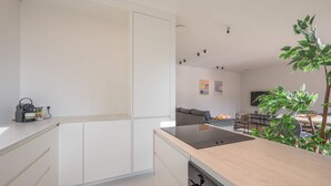 A modern kitchen with white cabinets, a black countertop, and a dining area with a table and chairs. - Levant Appartement 2 Slaapkamers 2 Badkamers Balkon Knokke-heist (Knokke-Heist)