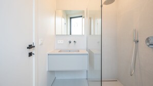 A modern bathroom with a glass shower enclosure, a white sink, and a large mirror. - Levant Appartement 2 Slaapkamers 2 Badkamers Balkon Knokke-heist (Knokke-Heist)
