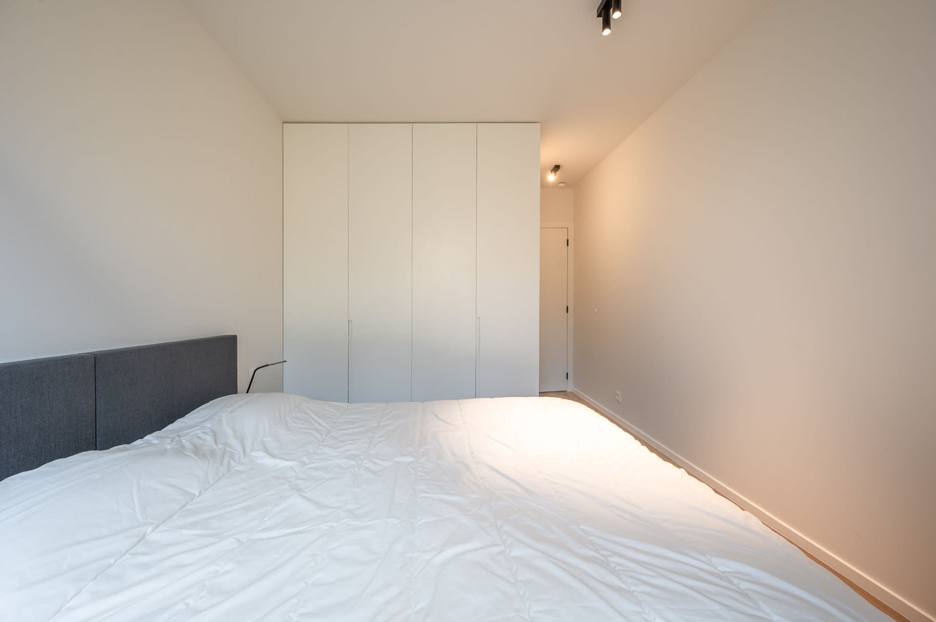 A bedroom with a bed, a grey headboard, and a wardrobe.