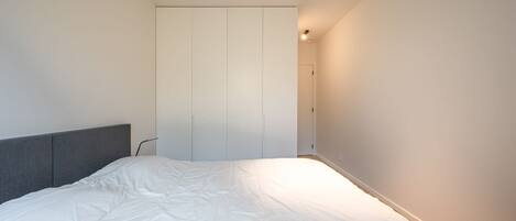 A bedroom with a bed, a grey headboard, and a wardrobe.