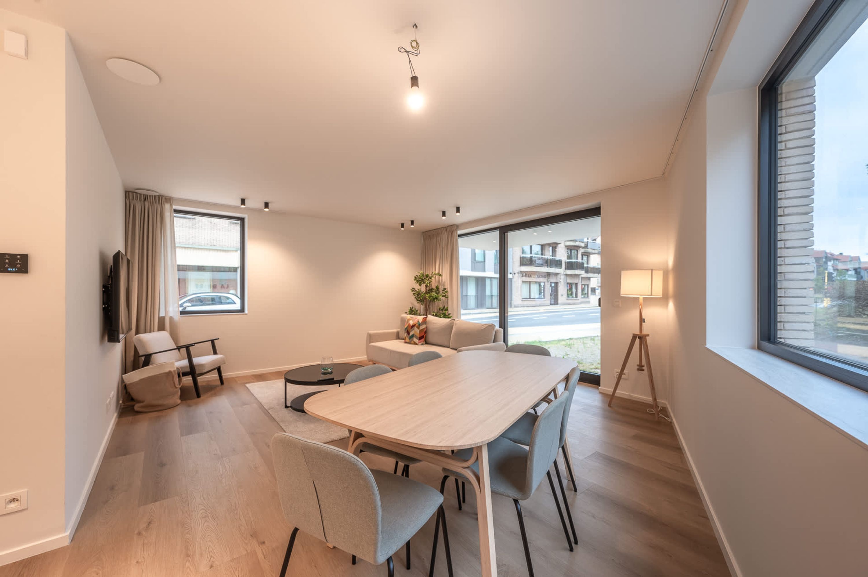 A modern hotel room with a large window, a dining table, comfortable seating, and a TV.