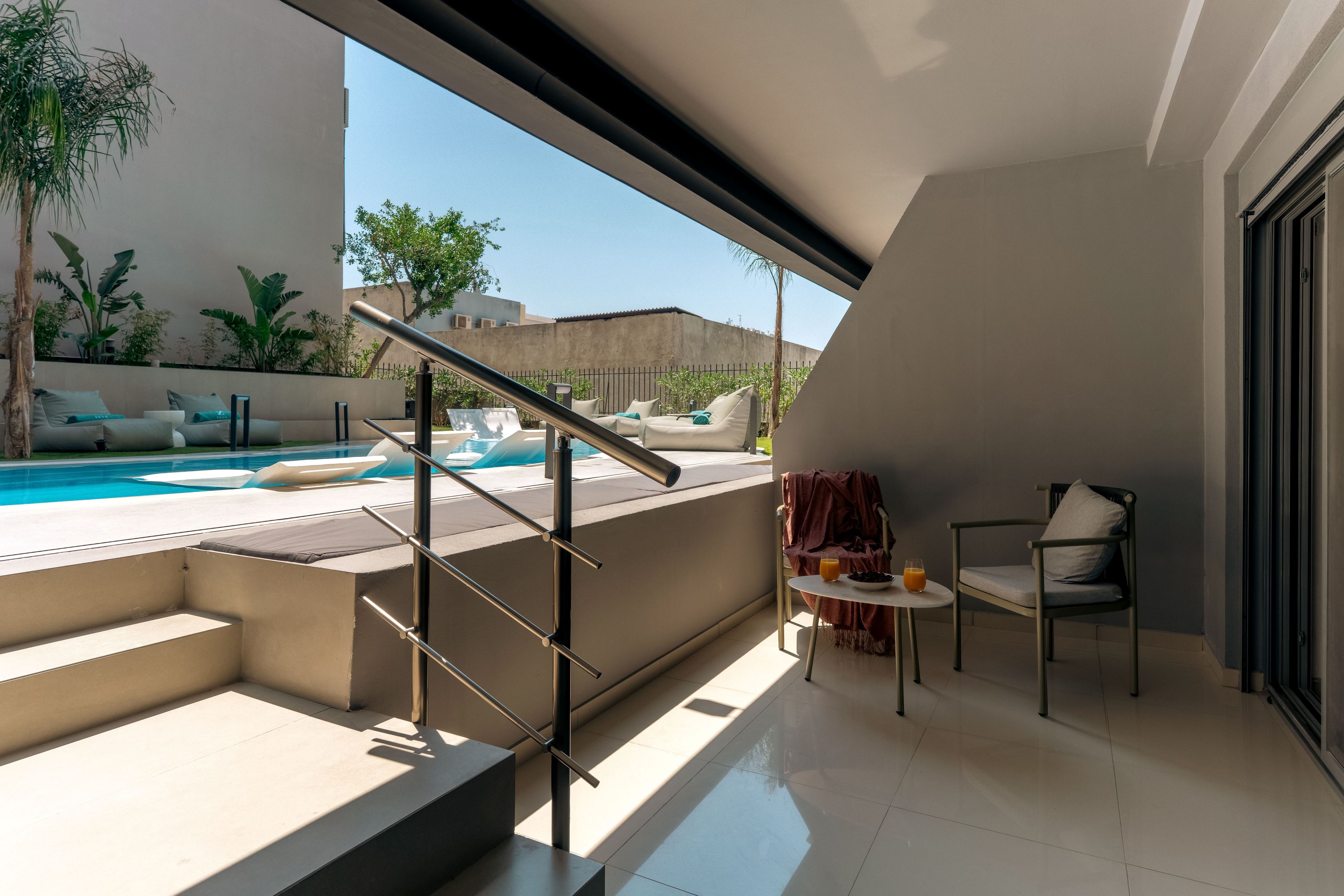 A modern outdoor balcony with a pool, a seating area with a table, and a staircase leading to an upper level.