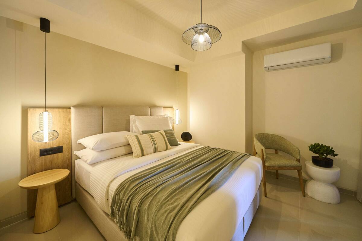 Une chambre à coucher comprenant un lit, une table de chevet, une chaise et un climatiseur fixé au mur.