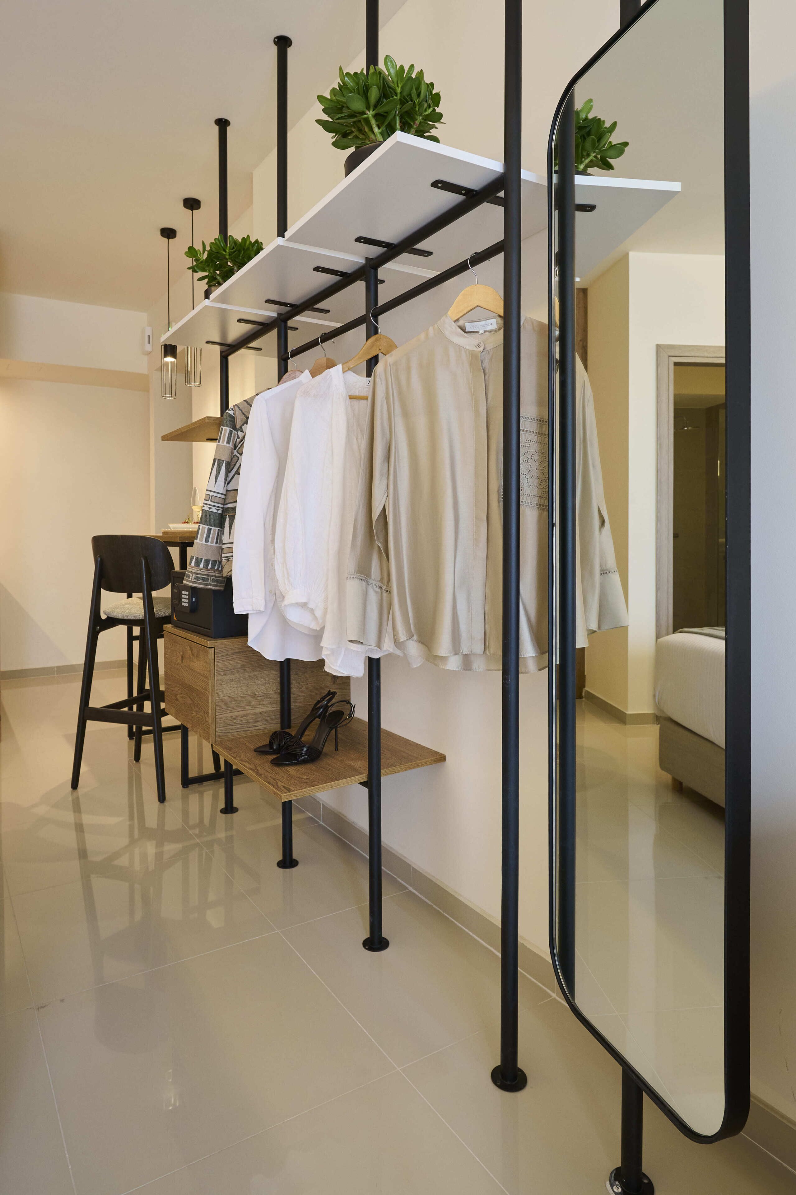 Une chambre moderne avec un miroir, un bureau en bois, une chaise, un portant à vêtements et un lit.