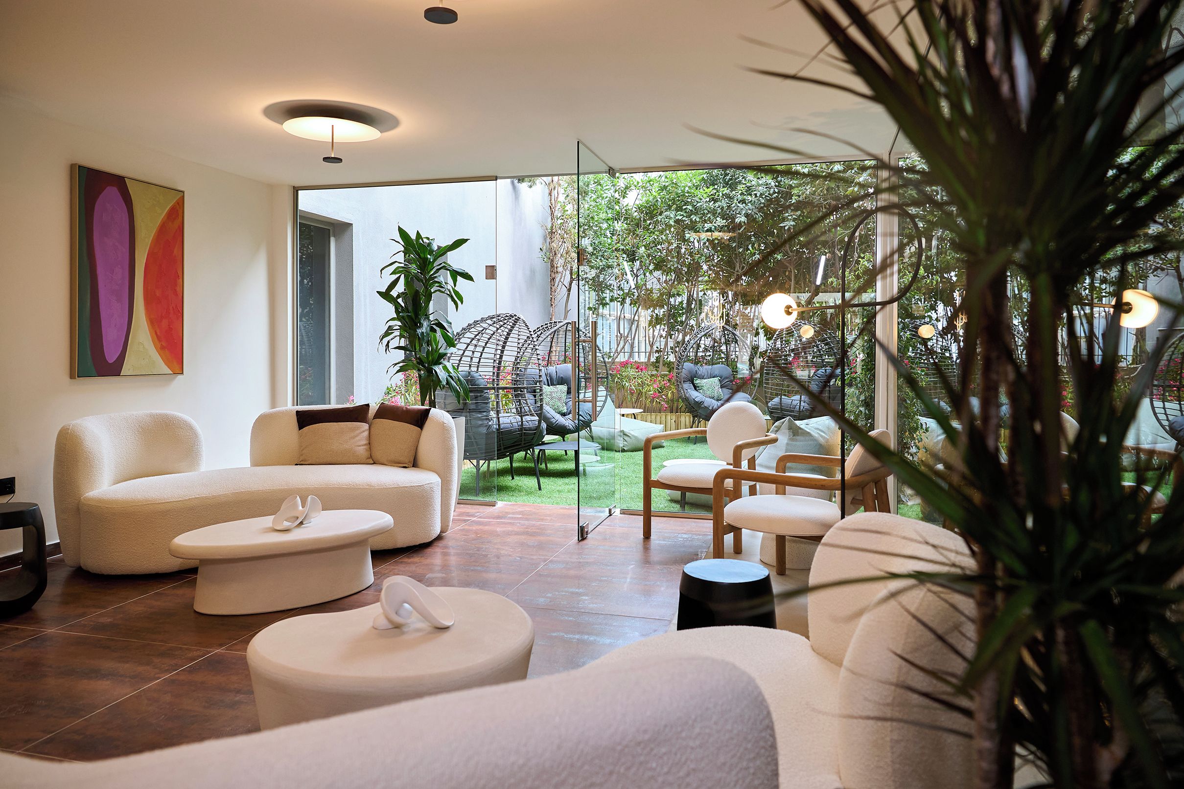 A modern living room with a sofa, chairs, and a coffee table. There is a large window providing a view of a garden.