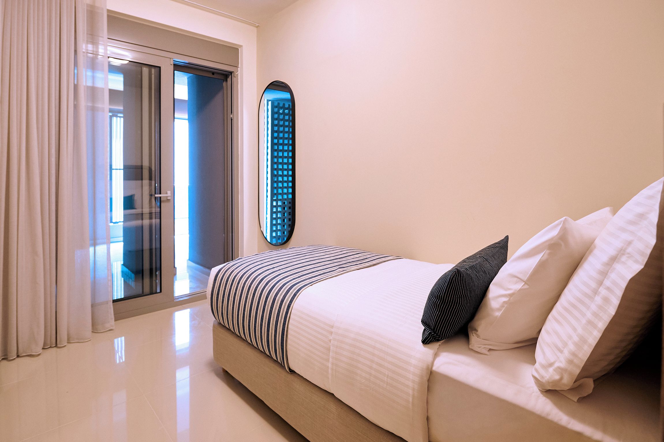 A hotel room with a bed, a large window, and a view of the cityscape.