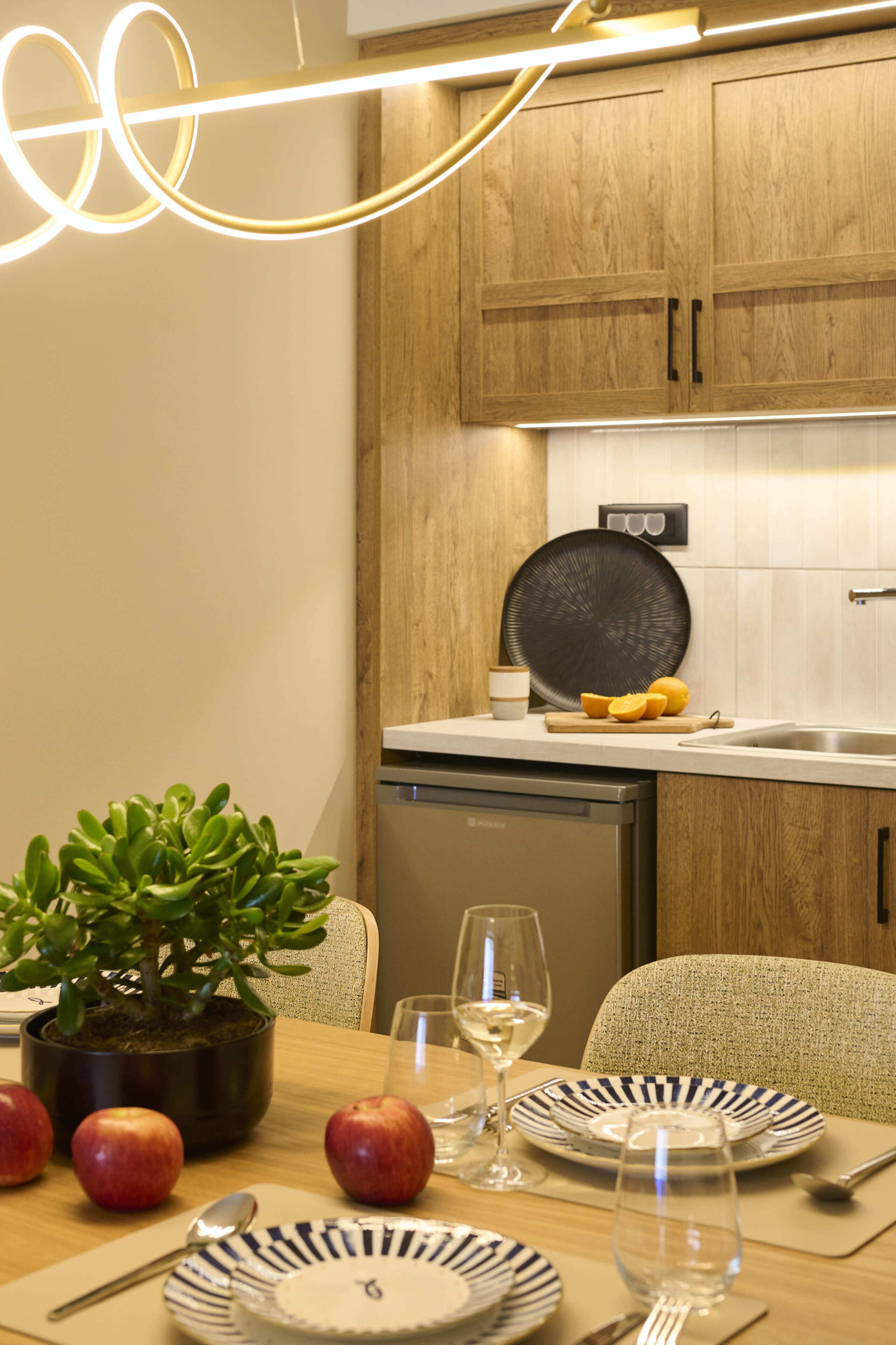 Una cocina moderna con armarios de madera, lavavajillas integrado y un comedor con platos, vasos y una planta en maceta.