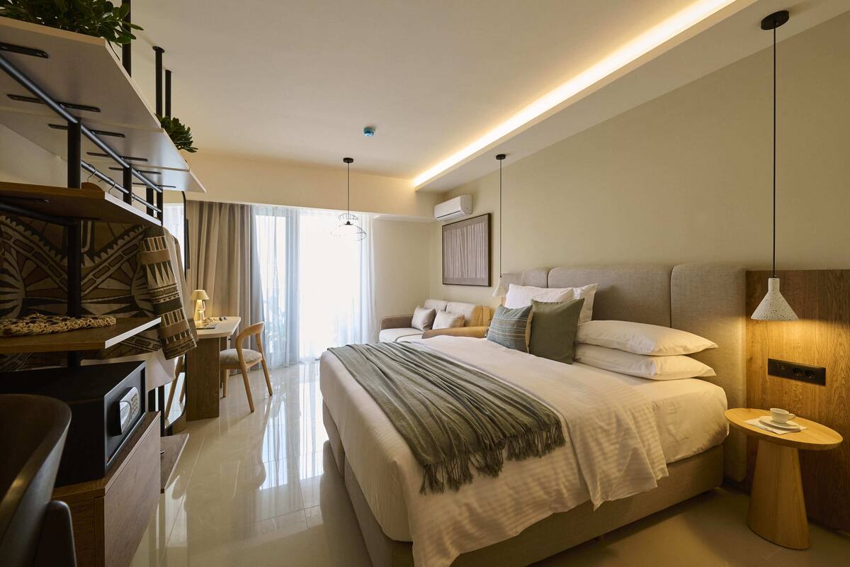 Une chambre d’hôtel moderne, équipée d’un lit, d’une table de chevet, d’une lampe et offrant une vue sur l’extérieur.
