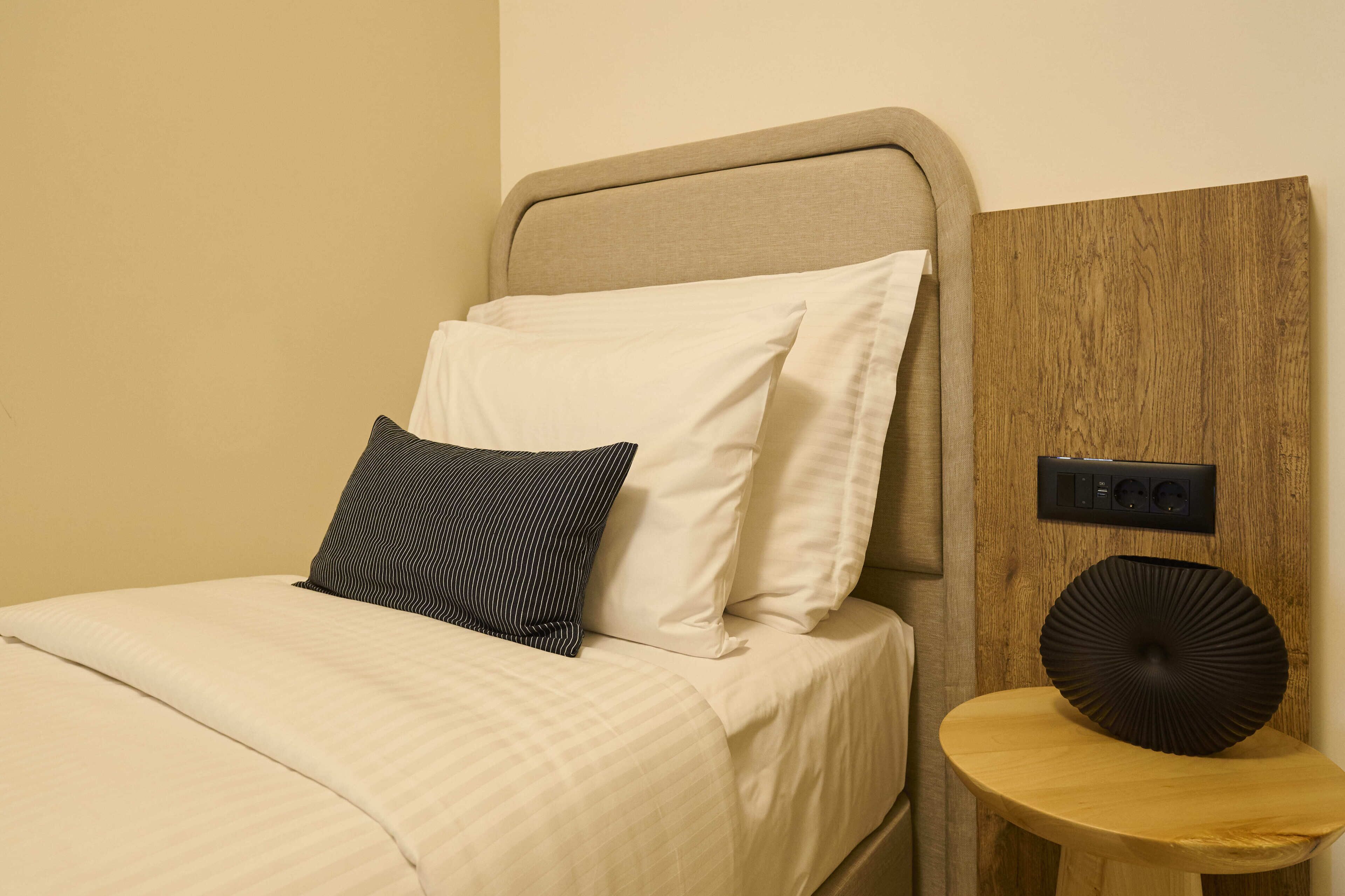A bed with a headboard, a bedside table with a decorative item, and a wall-mounted power outlet.