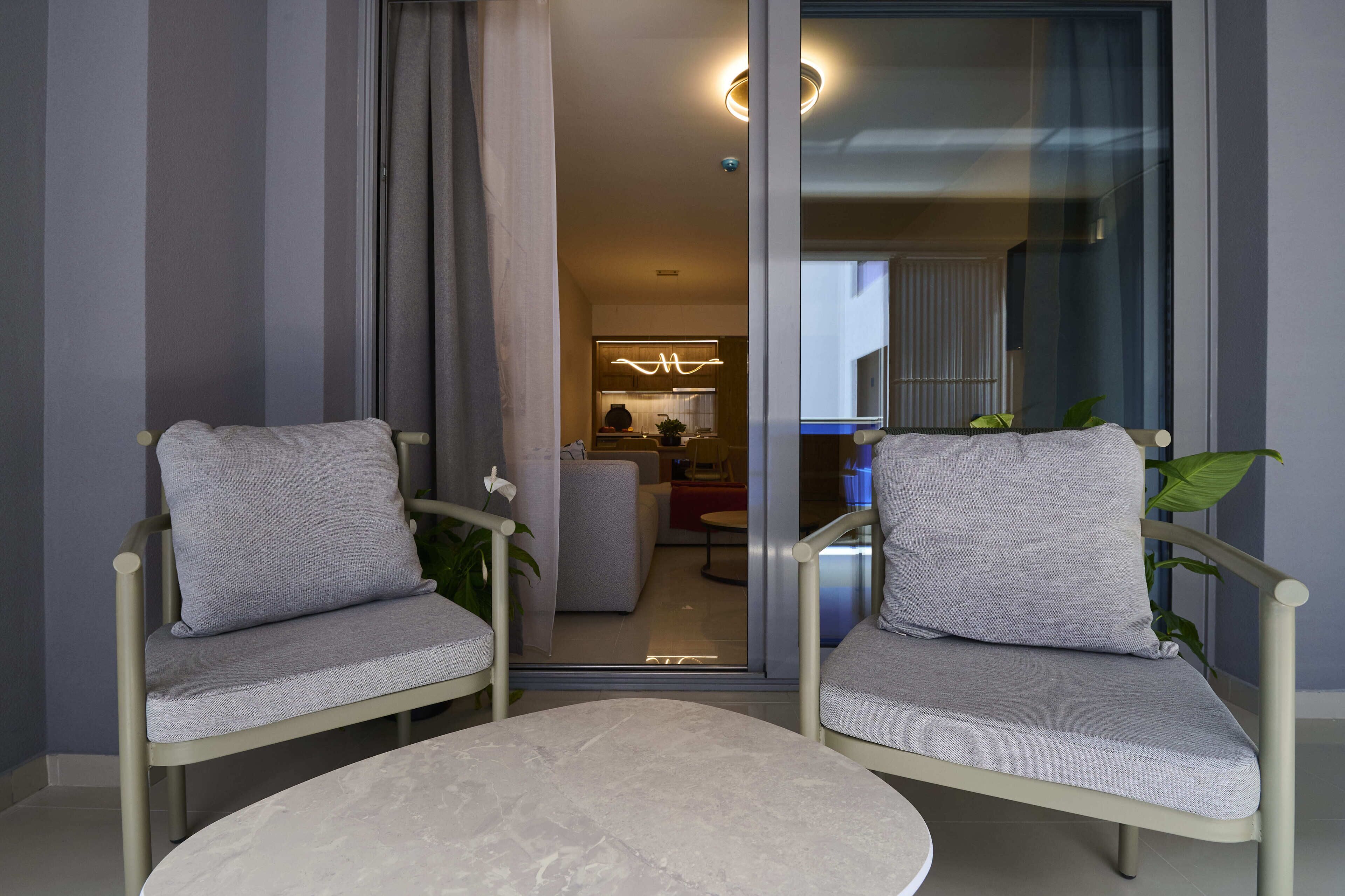 Ein modernes Wohnzimmer mit zwei grauen Polsterstühlen, einem runden Tisch und einer Glastür zum Küchenbereich.