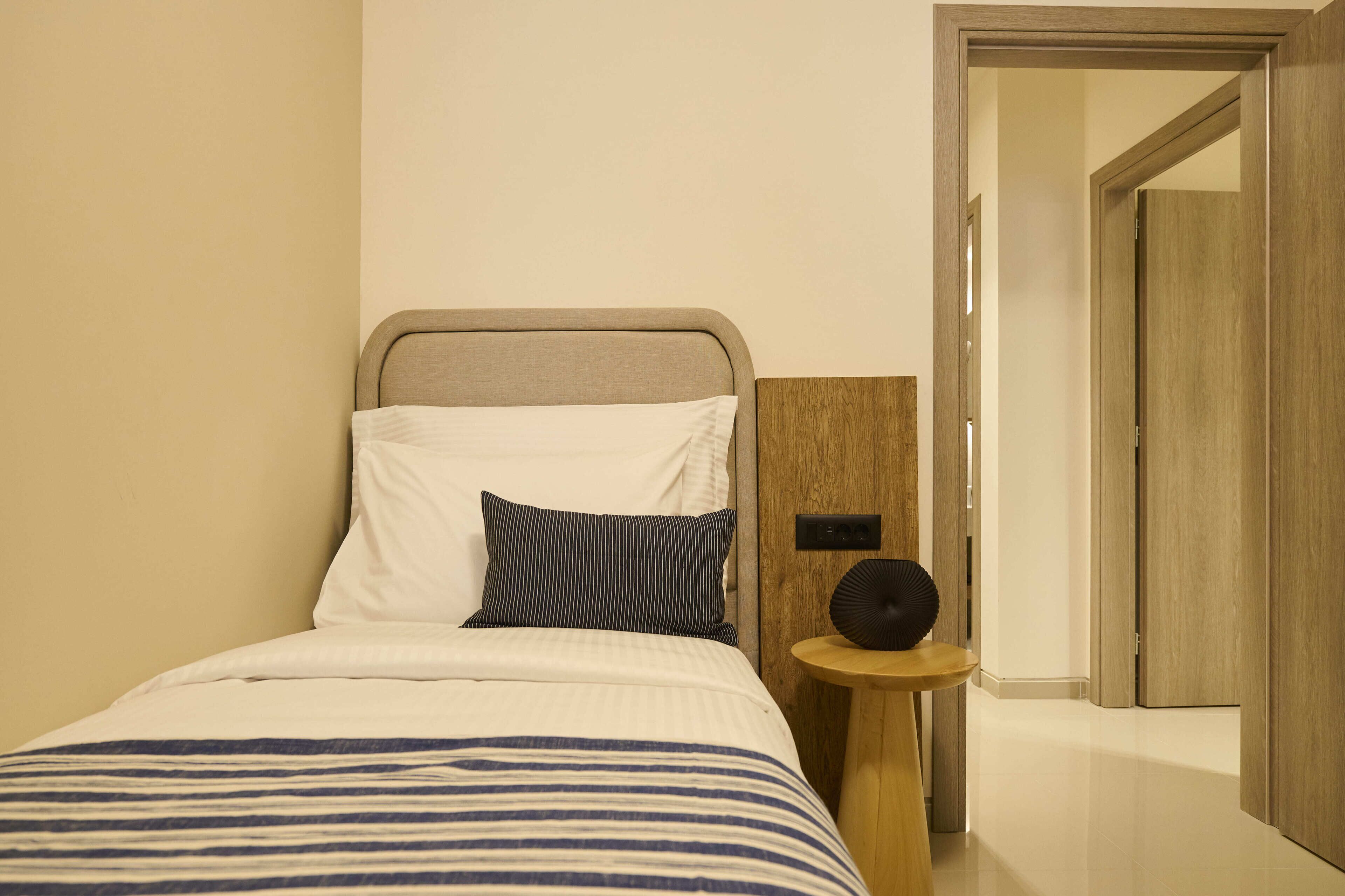 A neatly made bed with a striped bedspread, a pillow, and a bedside table with a round black object.