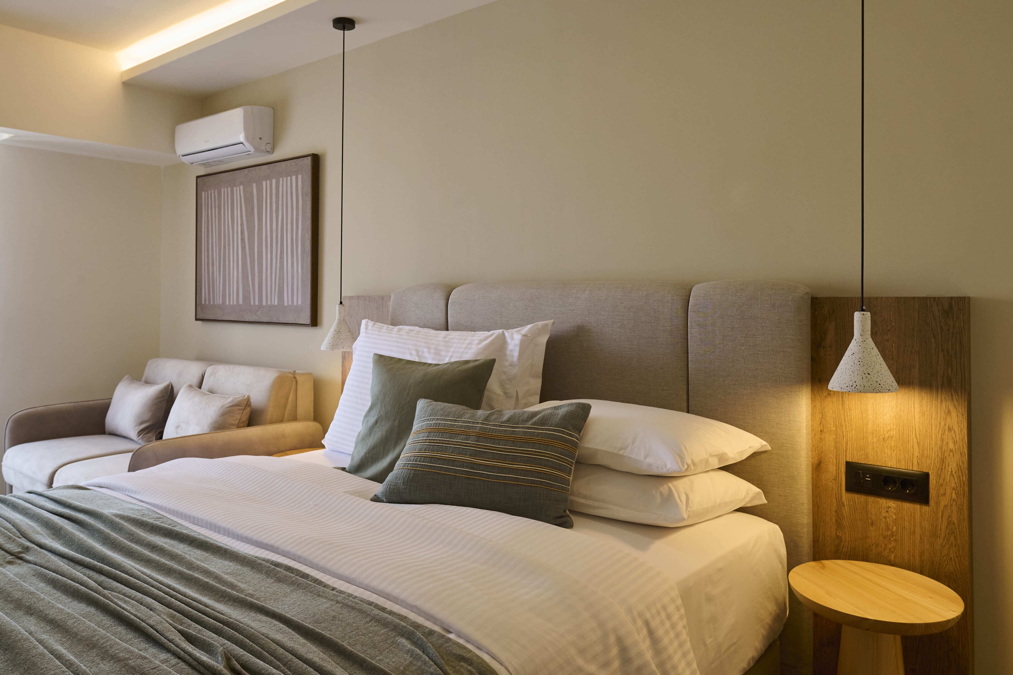 A modern hotel room with a bed, bedside table, and a wall-mounted air conditioner.