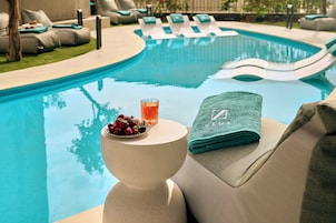 Zona de piscina con sillas de descanso, una cesta de bebidas y fruta sobre una mesa, y una toalla con un logotipo.