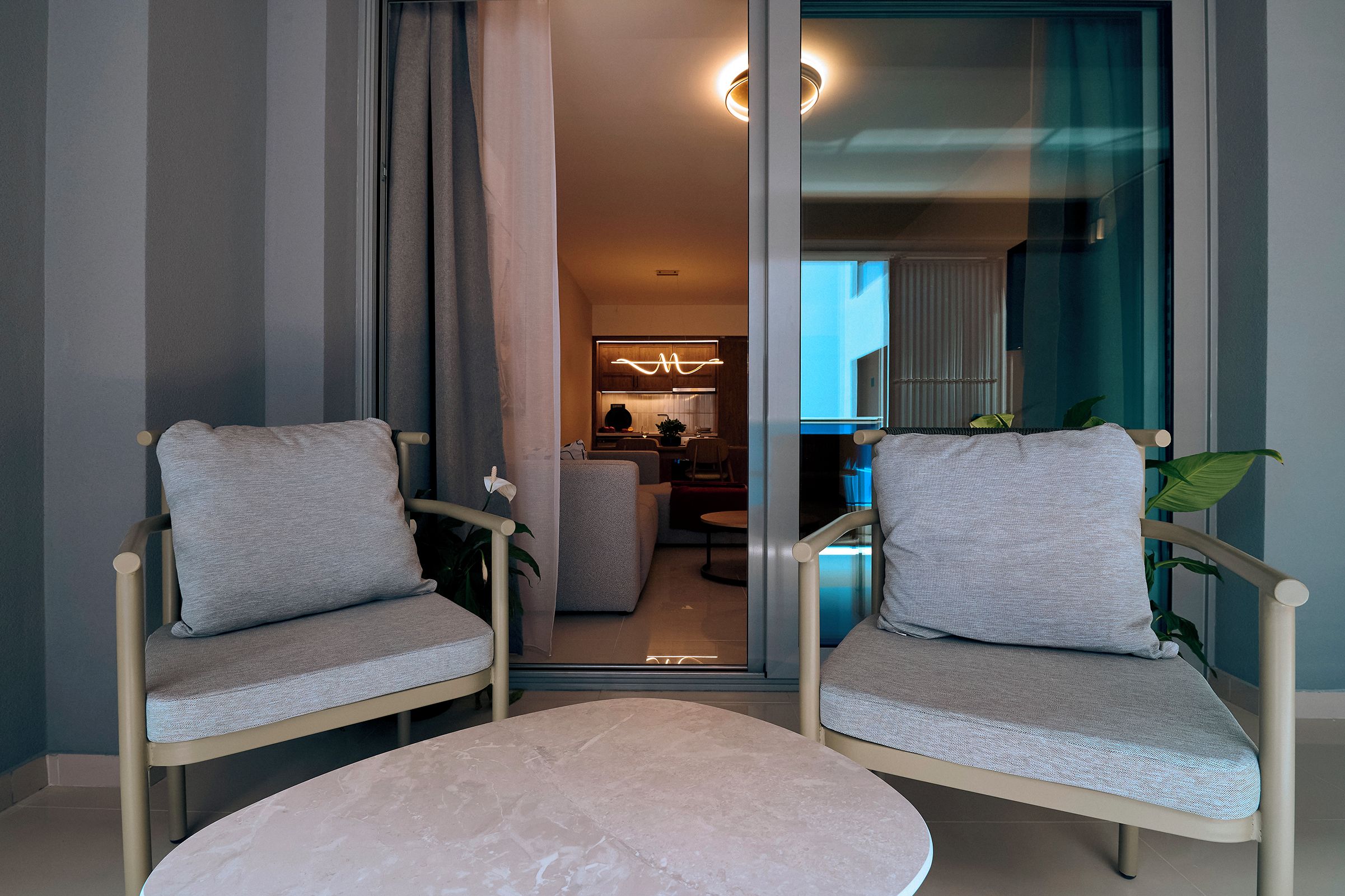 Ein modernes Wohnzimmer mit zwei grauen Polstersesseln, einem runden Tisch und einer Glastür zum Essbereich.