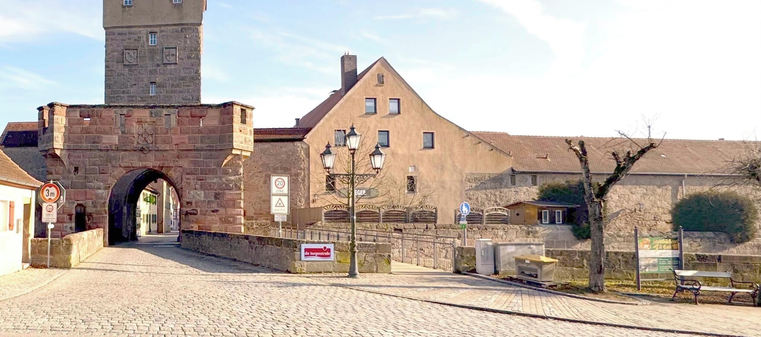 A cobblestone street leading to a historic building with a tower, a sign indicating a 20 zone, and a pedestrian crossing.