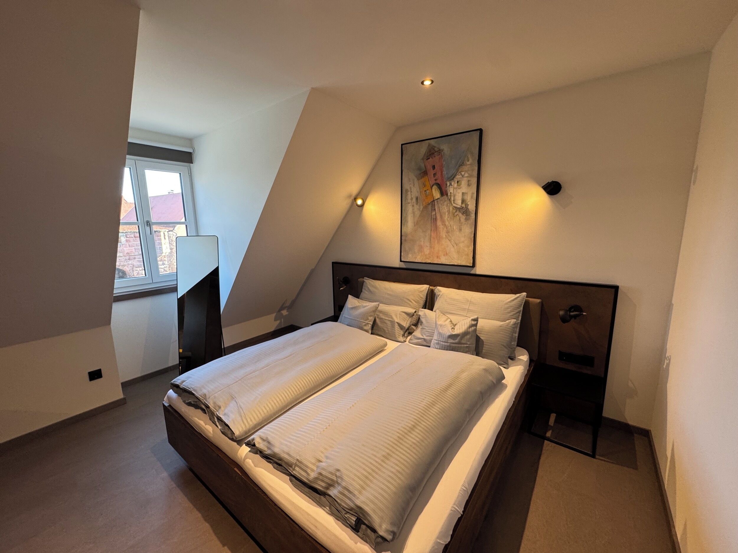 Een slaapkamer met een groot bed, een nachtkastje, een schilderij aan de muur en een raam.