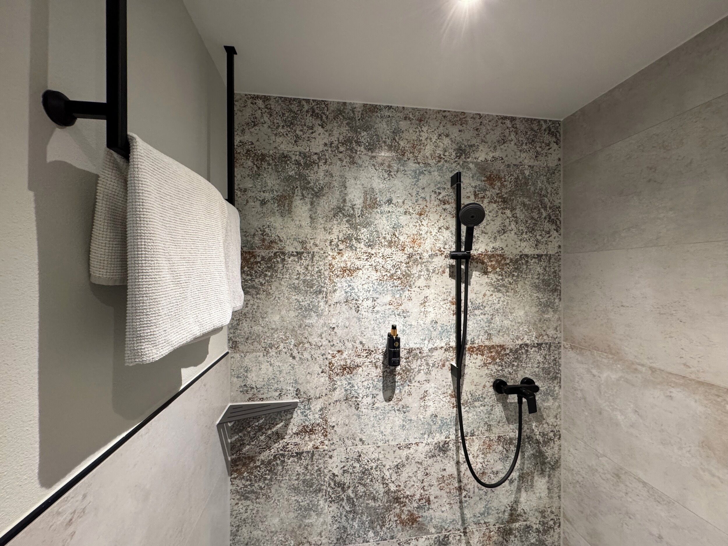 Un baño moderno con pared texturizada, un perchero y un sistema de ducha.