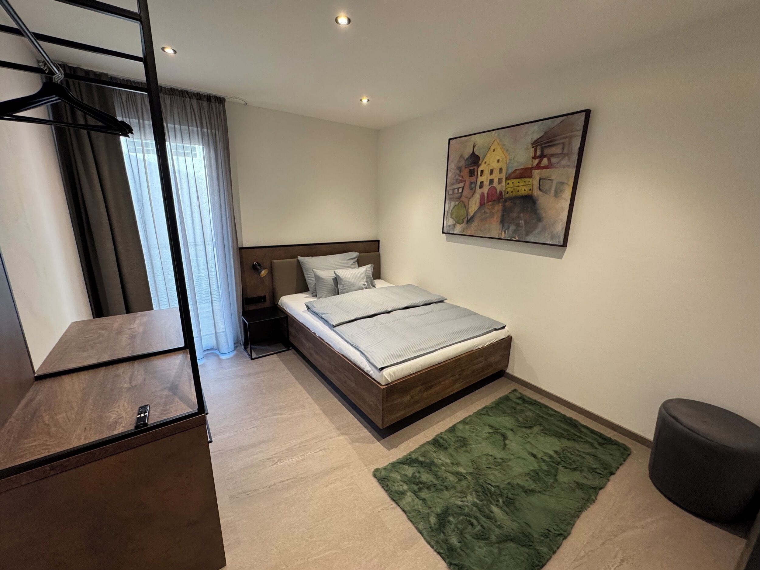 Un dormitorio moderno con una cama de madera, una alfombra verde, una mesita de noche y un cuadro en la pared.