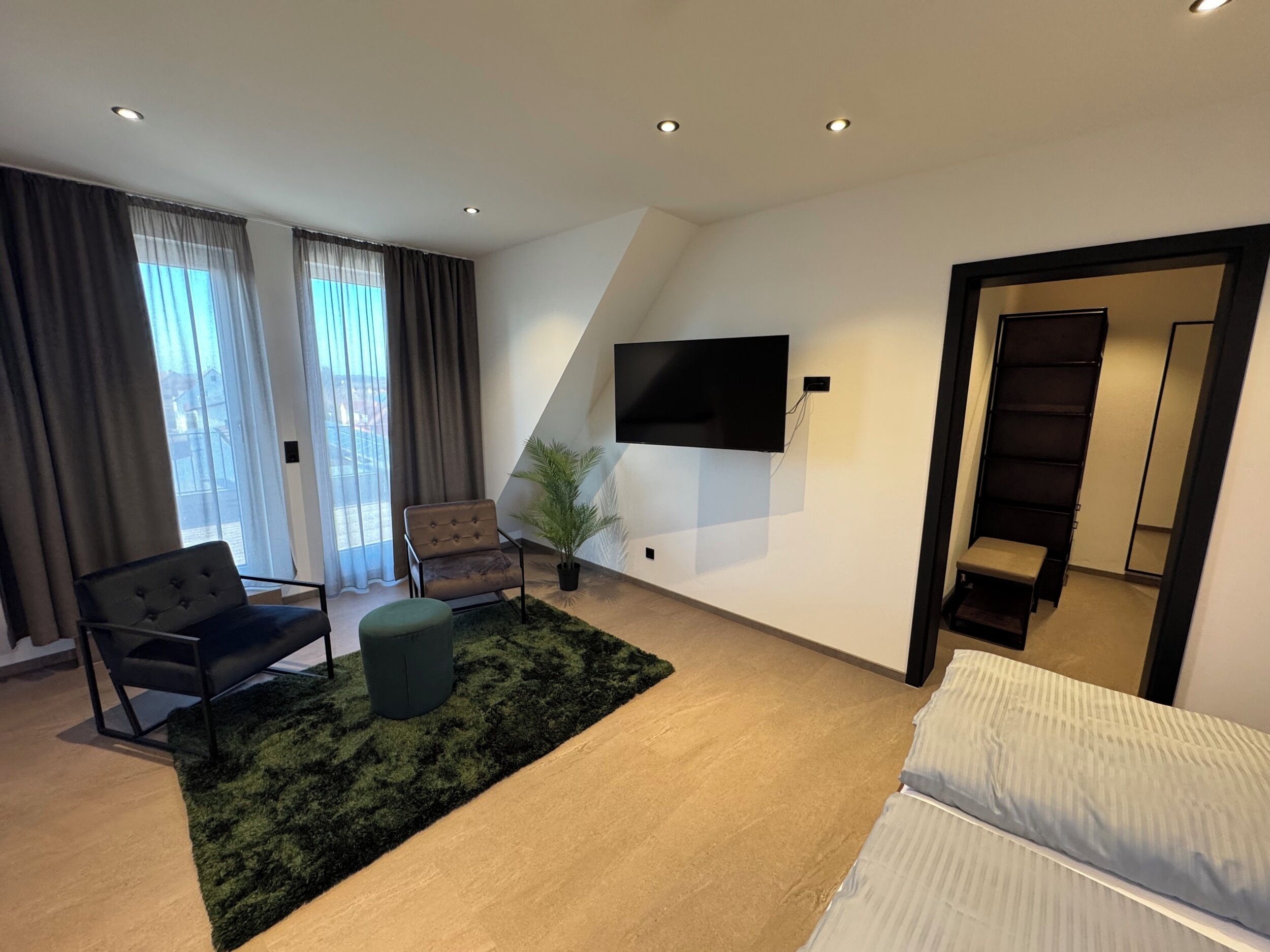 Una sala moderna con sofá, sillón, reposapiés y un televisor de pantalla plana montado en la pared.